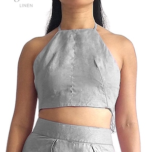 May include: A light grey linen halter top and matching skirt. The top has a simple design with a halter neck and a cropped length. The skirt appears to be high-waisted with a front slit. The text "bay bay" and "LINEN" is in the upper left corner.