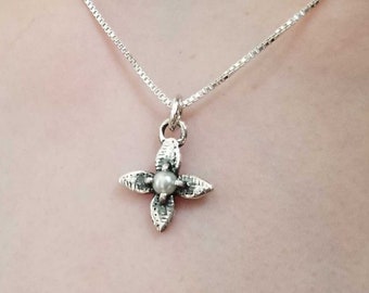 May include: A silver necklace with a delicate flower pendant featuring a small pearl in the center.