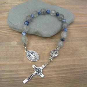 May include: A silver rosary with blue and white beads, a silver crucifix, and a silver medal of the Virgin Mary.