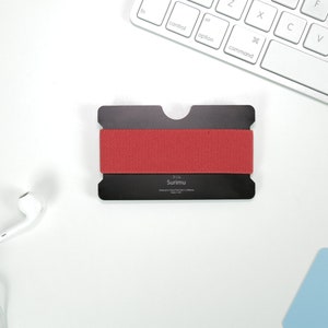 May include: A black metal card holder with a red elastic band. The card holder has the text "A Little Symmetry" printed on it.