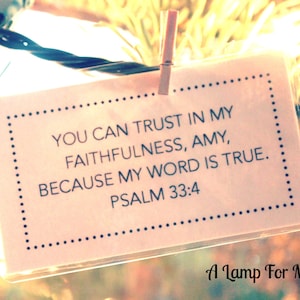May include: A white card with black text and a dotted border hangs from a string of lights. The card reads "You can trust in my faithfulness, Amy, because my word is true. Psalm 33:4". Below the card is the text "A Lamp For My Feet".