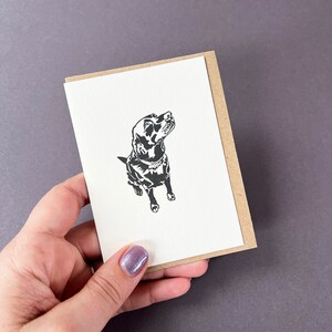 May include: A black and white illustration of a dog looking up, printed on a white card with a brown envelope.