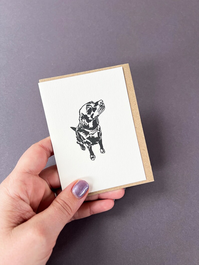 May include: A black and white illustration of a dog looking up, printed on a white card with a brown envelope.