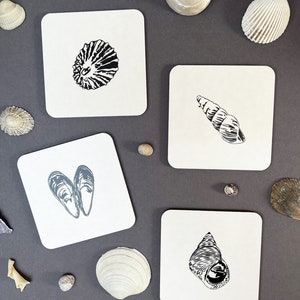 May include: Set of five square coasters with black and white illustrations of seashells. The coasters are made of a light brown material and have a smooth surface.