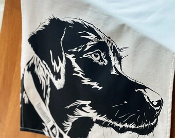 May include: A black and white illustration of a dog's head on a white tea towel. The dog is looking to the right and has a collar on.