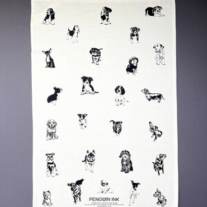 May include: A white tea towel featuring a black and white illustration of various dog breeds. The text "PENGUIN INK" is printed in the bottom centre of the towel.