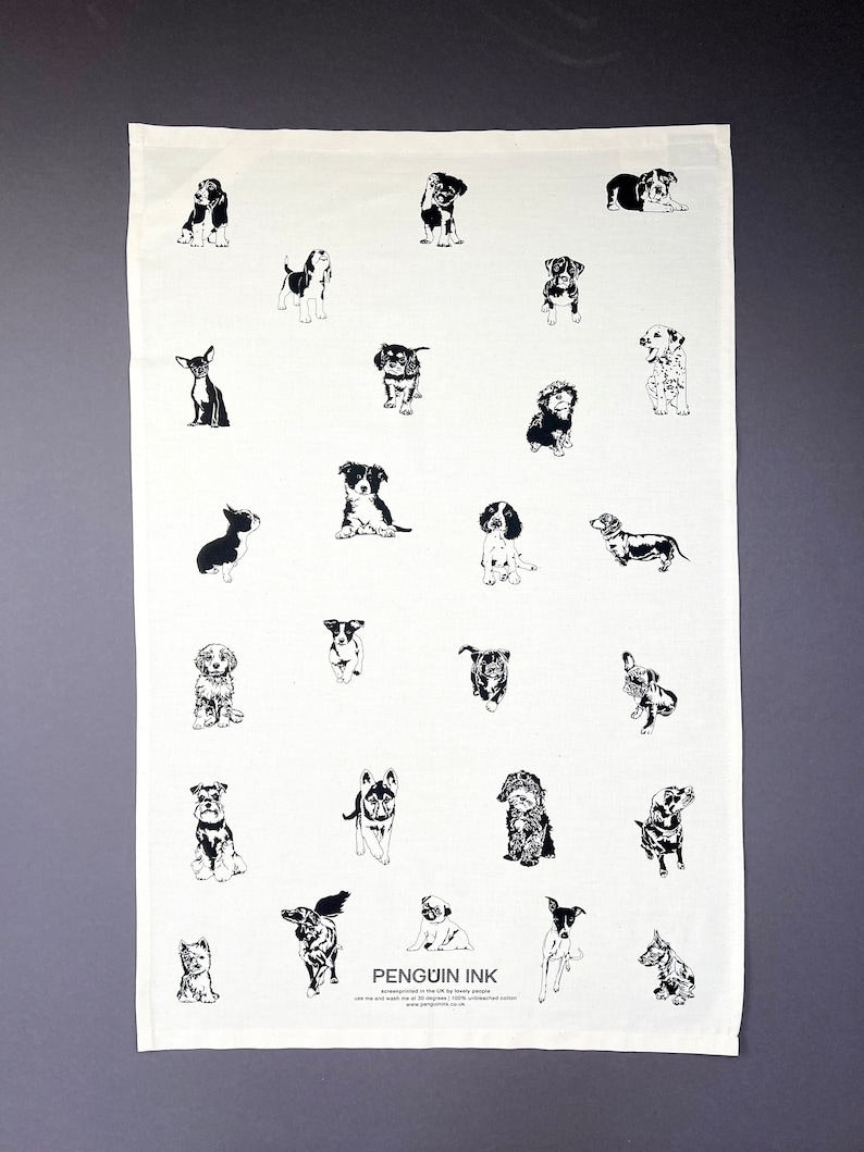 May include: A white tea towel featuring a black and white illustration of various dog breeds. The text "PENGUIN INK" is printed in the bottom centre of the towel.