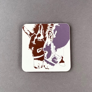 May include: A white coaster featuring a brown and purple silhouette of two donkeys' heads touching noses.