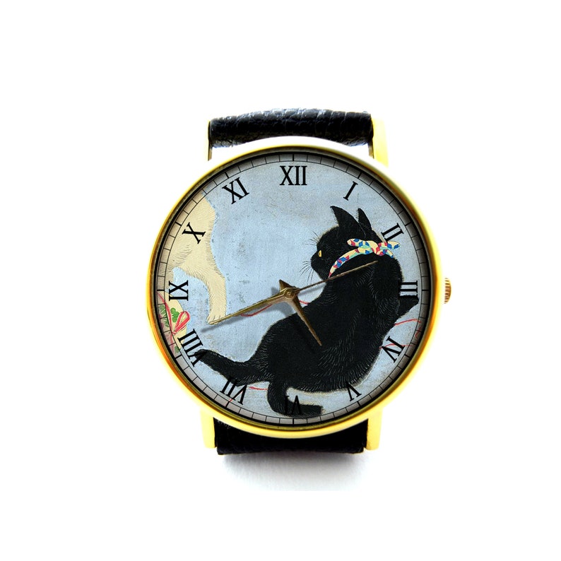 May include: A gold-tone wristwatch with a black leather band features a black cat with a colorful ribbon on a blue and white background. The watch face has Roman numeral hour markers.