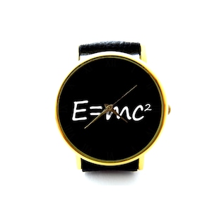 Puede incluir: Un reloj de pulsera dorado con una esfera negra y una correa de cuero negra. La esfera del reloj presenta la ecuación E=mc² escrita en blanco.
