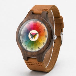 May include: A wristwatch with a dark brown wooden case and a tan leather strap. The watch face features a circular rainbow color wheel design with black Roman numerals and a central white circle containing a pink and yellow triangle icon.
