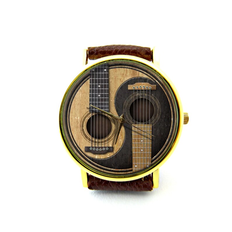 May include: A gold-tone wristwatch with a brown leather band features a yin-yang design with two acoustic guitars on the face.