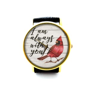 May include: A gold-tone wristwatch with a black leather band. The watch face features a white woodgrain background with a red cardinal and the text "I am always with you".