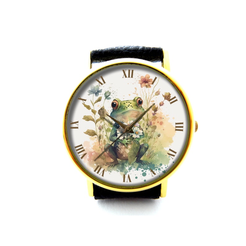 May include: A gold-tone wristwatch with a black leather band. The watch face features a watercolor illustration of a green frog holding a flower, surrounded by other flowers and greenery. The watch face also has Roman numeral hour markers.