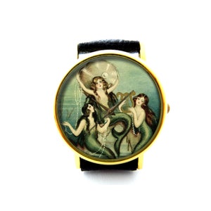 May include: A gold-tone wristwatch with a black leather strap features a vintage illustration of three mermaids playing music. The watch face has a blue, green, and white background.