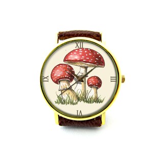 May include: A gold-tone wristwatch with a brown leather band features a white face with Roman numeral hour markers and a design of three red and white mushrooms with green foliage.