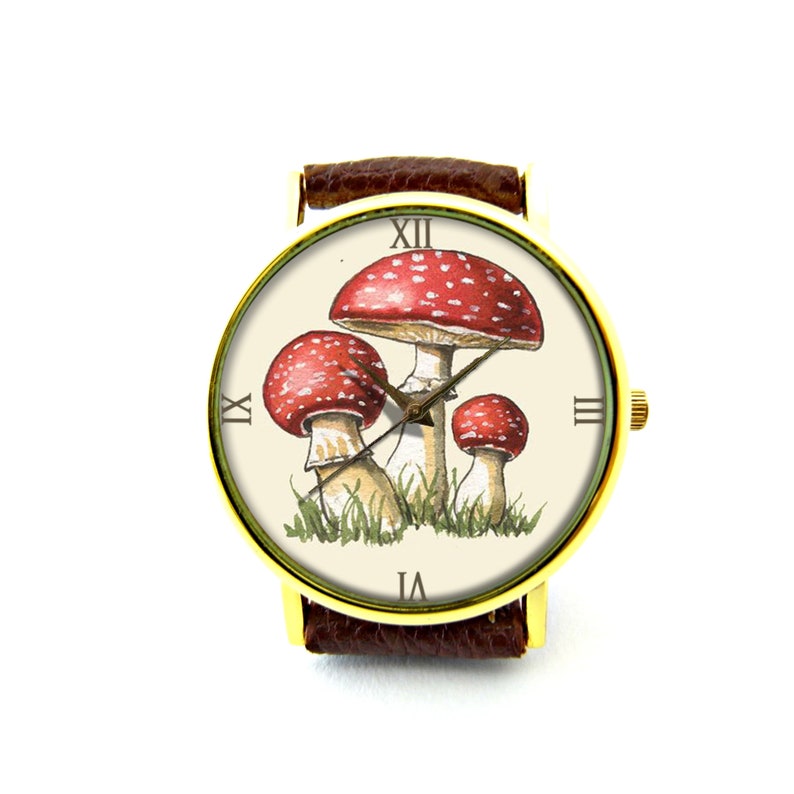 May include: A gold-tone wristwatch with a brown leather band features a white face with Roman numeral hour markers and a design of three red and white mushrooms with green foliage.