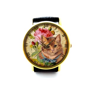 May include: A gold-tone wristwatch with a black leather strap features a vintage-style face with a floral design and a cat's face. The face has Roman numeral hour markers.
