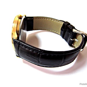 May include: A gold-tone wristwatch with a black leather band. The watch has a round face and a silver buckle.