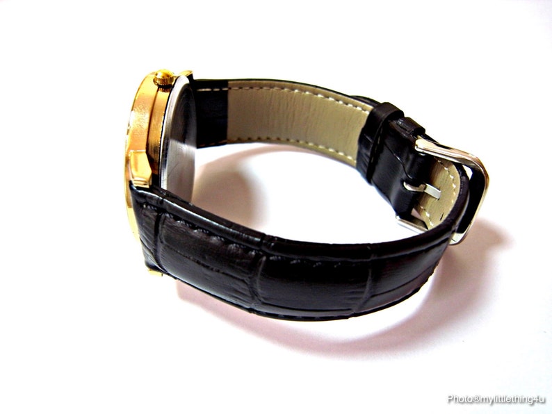 May include: A gold-tone wristwatch with a black leather band. The watch has a round face and a silver buckle.