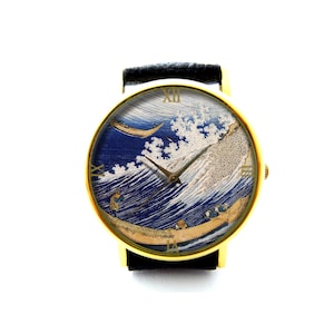 May include: A gold-tone wristwatch with a black leather strap. The watch face features a colourful image of "The Great Wave off Kanagawa" by Japanese artist Hokusai.