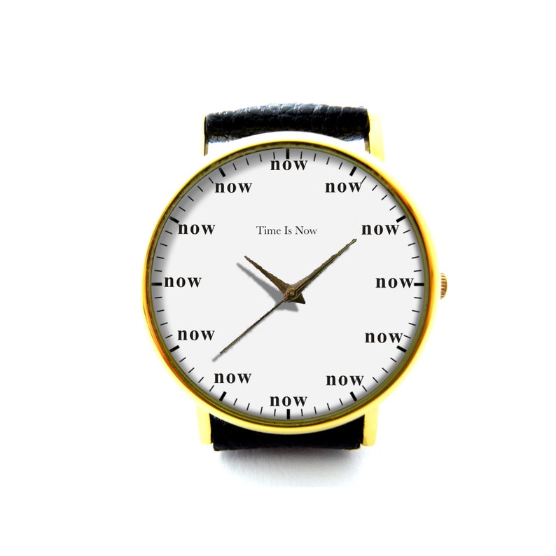 Peut inclure: Une montre-bracelet dor&eacute;e avec un cadran blanc. Le cadran de la montre comporte le mot "now" &agrave; la place des chiffres et le texte "Time Is Now". La montre a des bracelets en cuir noir.
