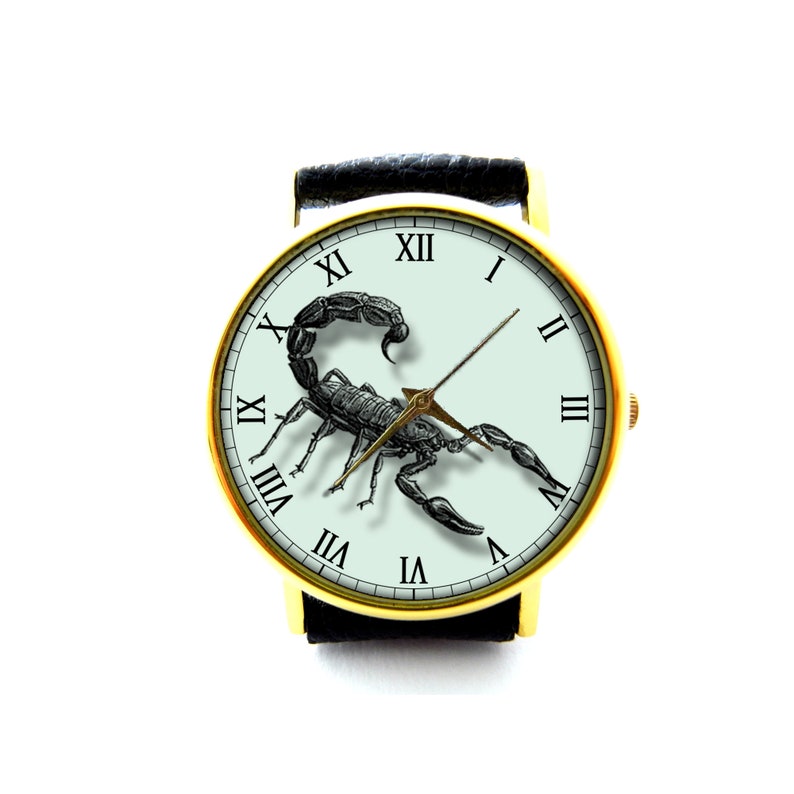 May include: A gold-tone wristwatch with a black leather band and a white face. The face features Roman numeral hour markers and a black scorpion illustration.