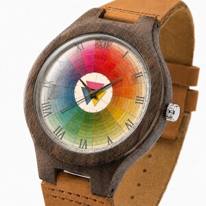 May include: A wristwatch with a dark brown wooden case and a tan leather strap. The watch face features a circular color wheel design with Roman numerals and a central white circle containing three small triangles in pink, blue, and yellow.