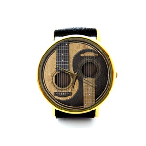 May include: A gold-tone wristwatch with a black leather band and a yin-yang design featuring two acoustic guitars. The watch face has a black and white yin-yang design with a brown acoustic guitar on each side.