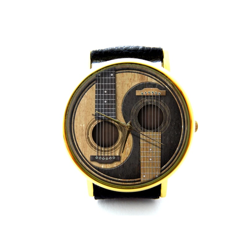 May include: A gold-tone wristwatch with a black leather band and a yin-yang design featuring two acoustic guitars. The watch face has a black and white yin-yang design with a brown acoustic guitar on each side.