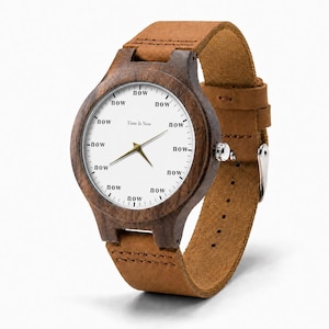 K&ouml;nnte beinhalten: Eine Holzarmbanduhr mit braunem Lederarmband. Das Zifferblatt ist wei&szlig; mit dem Wort "now" am Rand wiederholt. Der Text "Time Is Now" befindet sich in der Mitte. Die Uhr hat goldfarbene Zeiger.