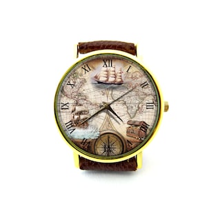 Pu&ograve; includere: Orologio da polso color oro con cinturino in pelle marrone. Il quadrante dell'orologio presenta un design a mappa vintage con velieri, una bussola e un forziere. I numeri romani segnano le ore.