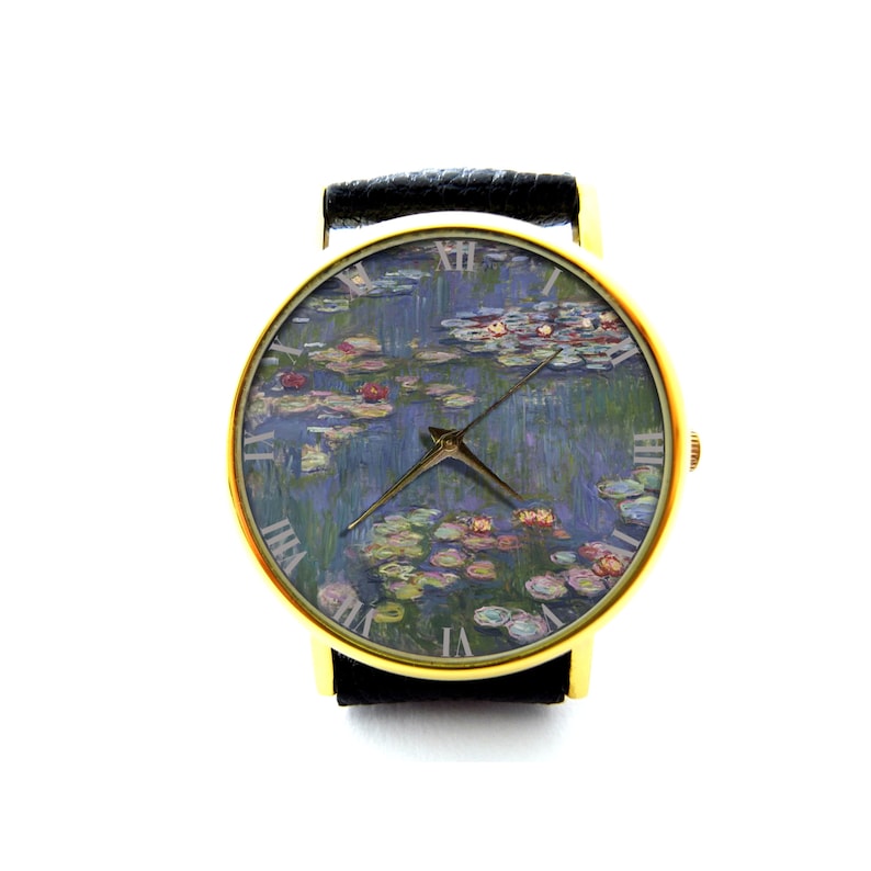 Puede incluir: Un reloj de pulsera dorado con una correa de cuero negro. La esfera del reloj presenta una pintura de nen&uacute;fares de Claude Monet.