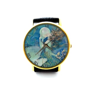 May include: A gold-tone wristwatch with a black leather strap. The watch face features a colourful illustration of a mermaid holding a pearl, surrounded by bubbles and fish.