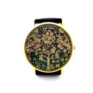 Puede incluir: Un reloj de pulsera dorado con una correa de cuero negro. La esfera del reloj presenta una impresión colorida de un árbol con pájaros y flores. Los números en la esfera del reloj son números romanos.