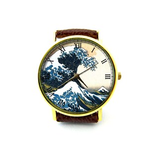 May include: A gold wristwatch with a brown leather band features a white face with Roman numeral hour markers and a depiction of the Great Wave off Kanagawa by Katsushika Hokusai.