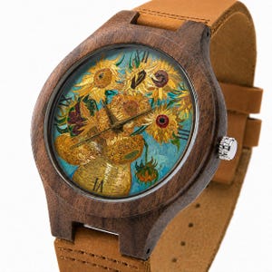 May include: Wooden wristwatch with a brown leather strap. The watch face features a painting of sunflowers in a vase, with gold hands and Roman numerals. The watch case is dark brown.