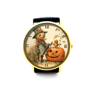 Peut inclure: Une montre dorée avec un bracelet en cuir noir présente une illustration vintage d'un épouvantail tenant une citrouille sculptée avec un petit oiseau perché sur le dessus. Le cadran de la montre comporte des chiffres romains pour les heures.