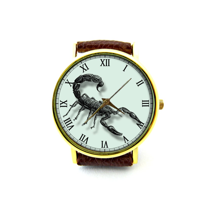 May include: A gold-tone wristwatch with a brown leather band features a white face with Roman numeral hour markers and a black scorpion illustration. The watch hands are gold-tone.