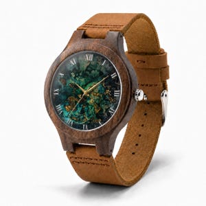May include: A wristwatch with a dark brown wooden case and a tan leather strap. The watch face features a deep green and black marbled pattern with gold-colored flecks, gold hands, and white Roman numeral hour markers around the circular dial.