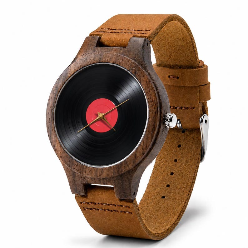 May include: A wooden wristwatch with a black vinyl record face and a red center. The watch has gold hands and a brown leather strap. The watch case is made of dark wood.