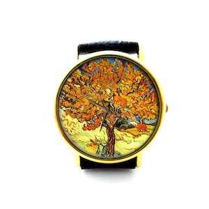 May include: A gold-coloured wristwatch with a black leather strap. The watch face displays a painting of a tree with orange and yellow leaves, in the style of Van Gogh. The watch has a classic design.