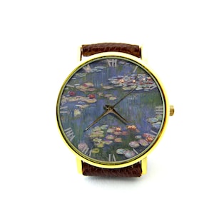 Puede incluir: Un reloj de pulsera dorado con una correa de cuero marr&oacute;n. La esfera del reloj presenta una pintura de nen&uacute;fares de Claude Monet.