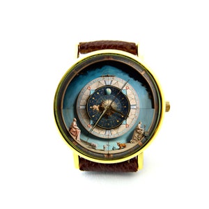 May include: A gold-tone wristwatch with a brown leather band. The watch face features a detailed illustration of a celestial sphere with zodiac symbols and planets.