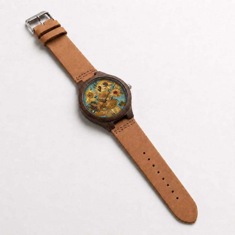 May include: A wristwatch with a brown leather band and a wooden watch face. The watch face features a painting of sunflowers in yellow, brown, and blue. The watch has a silver buckle.