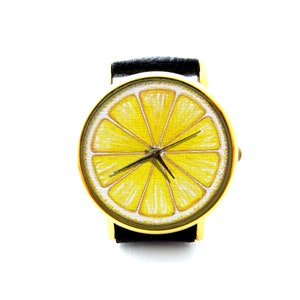 Pode incluir: Um rel&oacute;gio de pulso dourado com uma pulseira de couro preto e um design de fatia de lim&atilde;o no mostrador.