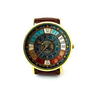 Pu&ograve; includere: Un orologio da polso dorato con un cinturino in pelle marrone. Il quadrante dell'orologio presenta un design dettagliato e colorato con numeri romani e un motivo circolare.