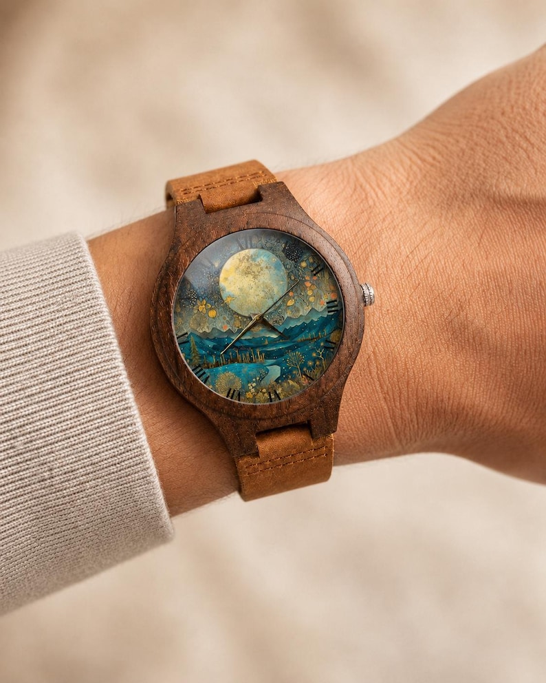 May include: A wooden wristwatch featuring a dark brown circular frame and a tan leather strap. The watch face displays a detailed illustration of a full moon over a blue mountain landscape with golden trees, gold hands, and black Roman numerals.