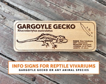 May include: A wooden sign with a brown background and white text. The sign features a line drawing of a gargoyle gecko and the text "GARGOYLE GECKO Rhacodactylus auriculatus". Below the drawing is information about the gargoyle gecko, including its range, diet, behaviour, lifespan, and length. The sign also includes the text "INFO SIGNS FOR REPTILE VIVARIUMS GARGOYLE GECKO OR ANY ANIMAL SPECIES".