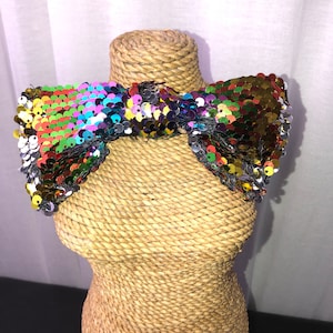 Peut inclure: Un nœud papillon pailleté multicolore avec un dos noir. Le nœud papillon est présenté sur un mannequin en paille.